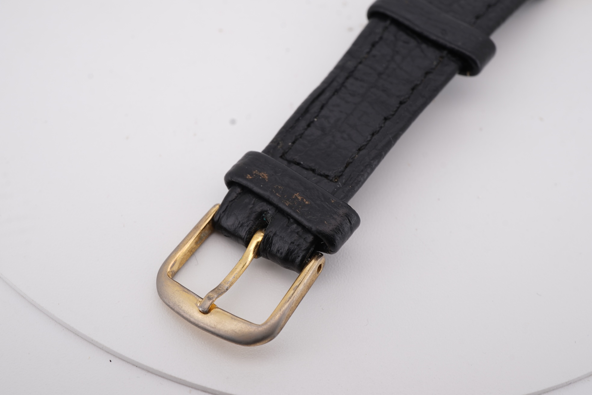 A gentleman's yellow metal Garrard manual wind wrist watch, with baton numerals and date aperture, case diameter 34mm, on a black leather strap.